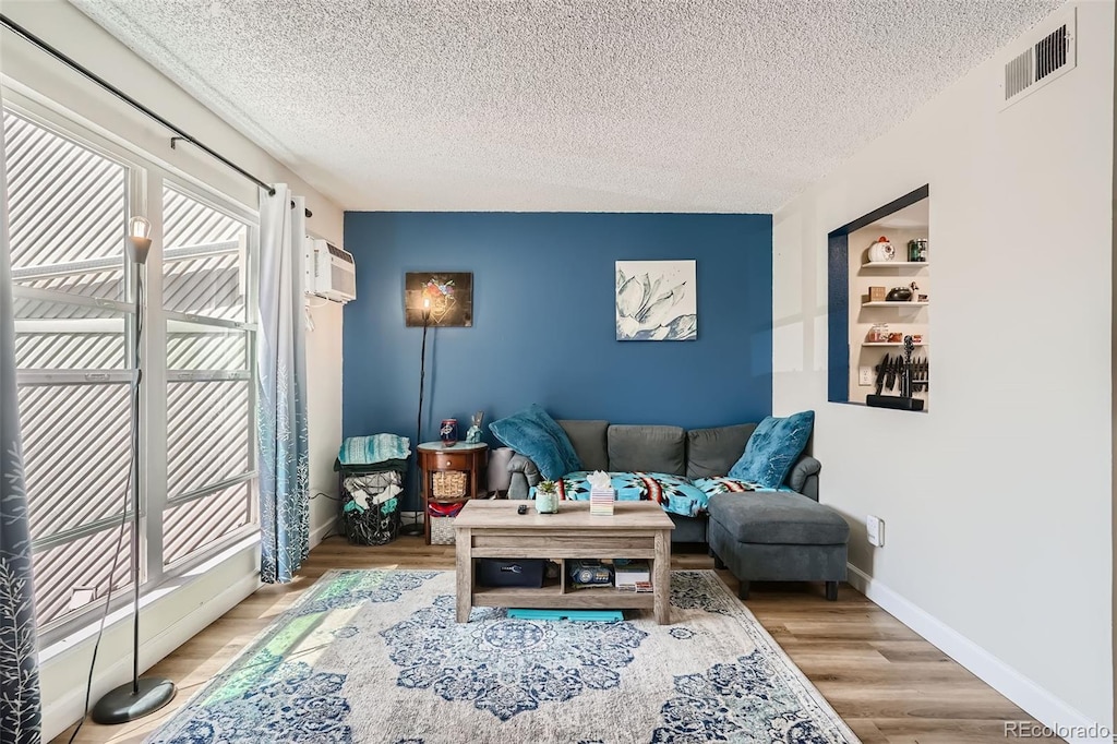 living room with light wood-type flooring, a textured ceiling, and a wall unit AC