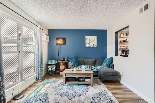 living room with light wood-type flooring, a textured ceiling, and a wall unit AC