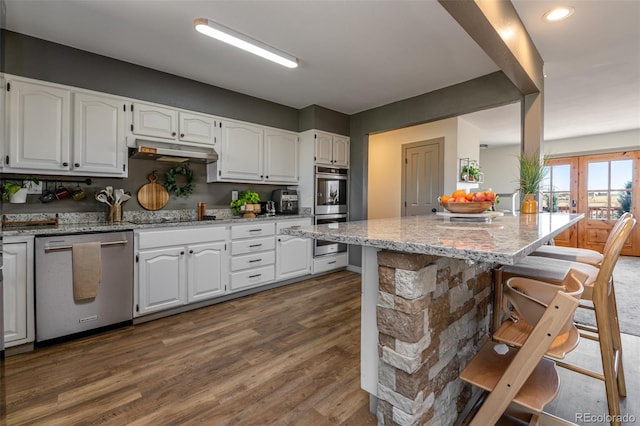 11170 Peaceful Valley Rd, Colorado Springs, CO 80925 - kitchen featuring appliances with stainless steel finishes, under cabinet range hood, a breakfast bar, white cabinets, and light stone countertops