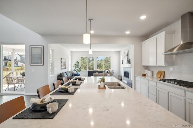 kitchen with gas stovetop, a sink, a glass covered fireplace, wall chimney exhaust hood, and open floor plan