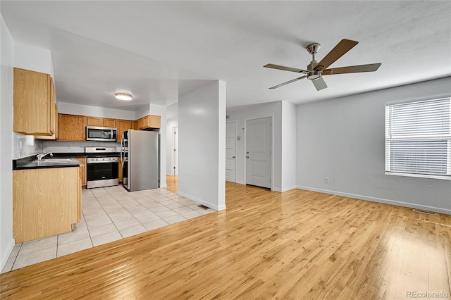 kitchen featuring appliances with stainless steel finishes, sink, light wood-type flooring, backsplash, and ceiling fan