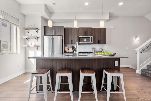 kitchen with a sink, a breakfast bar, dark brown cabinetry, baseboards, and appliances with stainless steel finishes