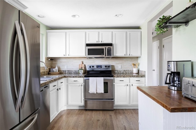 kitchen featuring appliances with stainless steel finishes, a sink, butcher block counters, decorative backsplash, and white cabinets