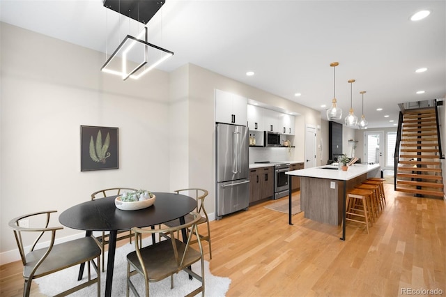 2179 S Bannock St, Denver, CO 80223 - kitchen featuring stainless steel appliances, white cabinetry, light countertops, a kitchen breakfast bar, and light wood-type flooring