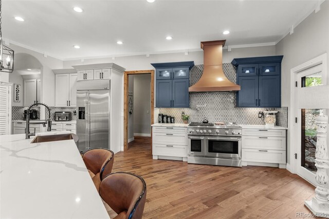 kitchen featuring light hardwood / wood-style floors, high end appliances, custom exhaust hood, and blue cabinets