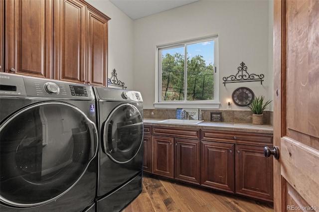 clothes washing area featuring cabinets, wood-type flooring, sink, and washer and clothes dryer