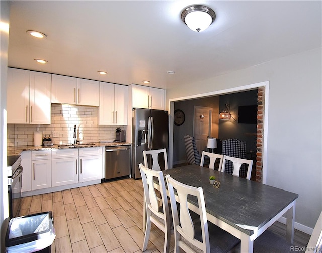 kitchen with appliances with stainless steel finishes, light wood-type flooring, light stone counters, sink, and white cabinets