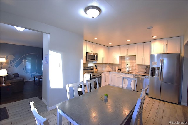 kitchen featuring white cabinetry, sink, stainless steel appliances, light hardwood / wood-style flooring, and decorative backsplash