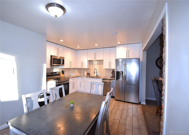 kitchen with decorative backsplash, white cabinetry, stainless steel appliances, and light hardwood / wood-style flooring