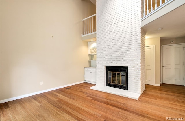 725 Crown Point Dr, Colorado Springs, CO 80906 - unfurnished living room featuring baseboards, wood finished floors, a brick fireplace, and a towering ceiling