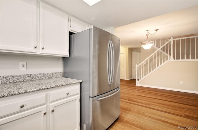 725 Crown Point Dr, Colorado Springs, CO 80906 - kitchen featuring freestanding refrigerator, light wood-style floors, white cabinets, pendant lighting, and light stone counters