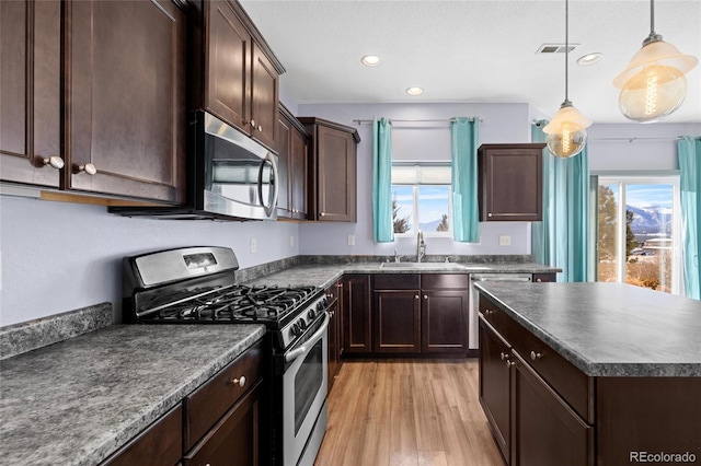 kitchen featuring dark brown cabinetry, decorative light fixtures, stainless steel appliances, sink, and light wood-type flooring