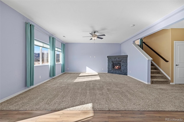 unfurnished living room with ceiling fan, a stone fireplace, and carpet