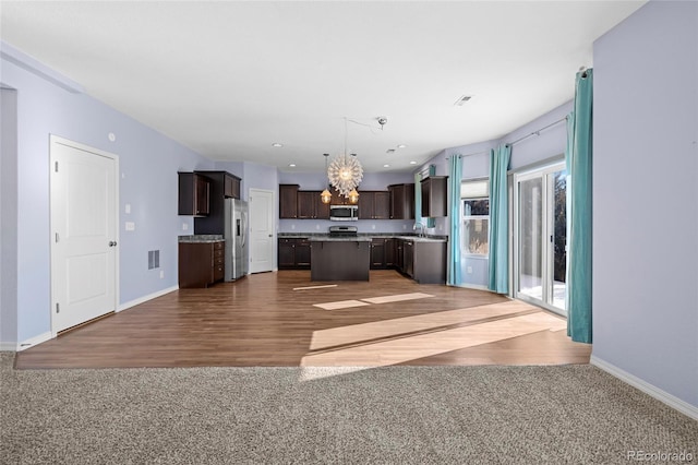 kitchen featuring appliances with stainless steel finishes, a center island, an inviting chandelier, and dark colored carpet