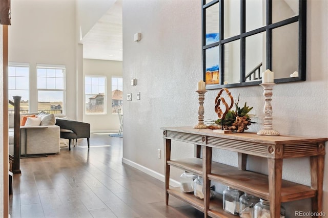 hallway featuring wood finished floors, baseboards, a high ceiling, and a textured wall