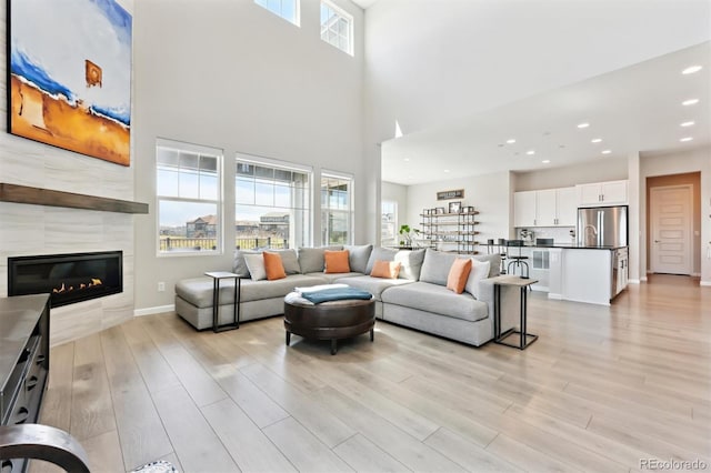 living room with recessed lighting, a tile fireplace, baseboards, a towering ceiling, and light wood-style floors