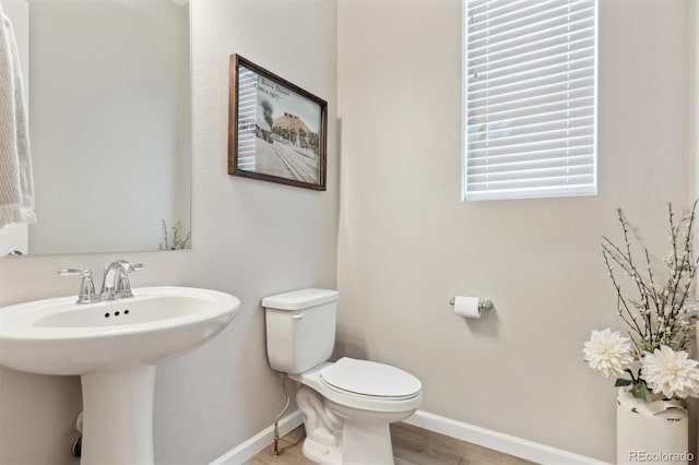bathroom featuring toilet, baseboards, wood finished floors, and a sink