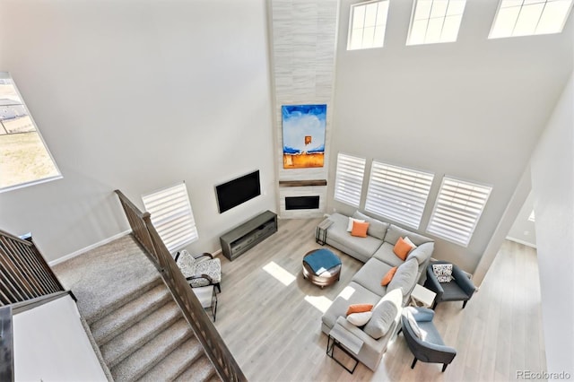 living room featuring a large fireplace, wood finished floors, baseboards, and a high ceiling