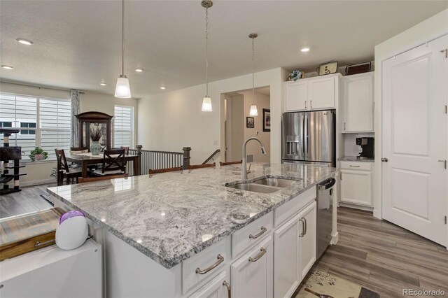 kitchen with white cabinetry, a kitchen island with sink, stainless steel appliances, decorative light fixtures, and sink