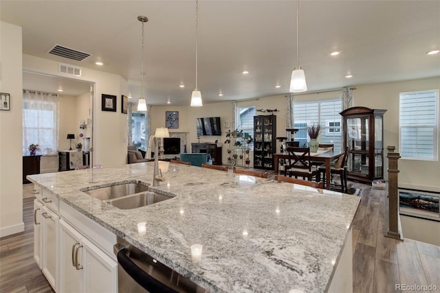 kitchen with sink, light stone counters, decorative light fixtures, white cabinets, and an island with sink