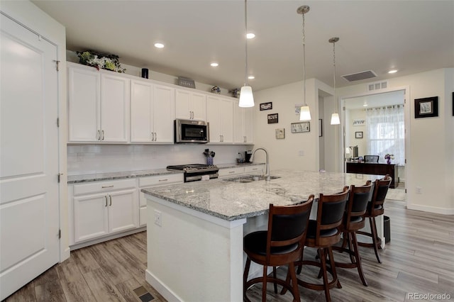 kitchen with hanging light fixtures, an island with sink, stainless steel appliances, and sink