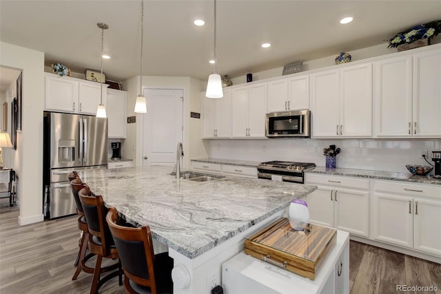 kitchen with a center island with sink, sink, white cabinetry, stainless steel appliances, and hanging light fixtures