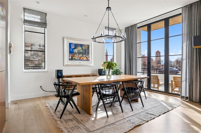 dining area featuring light wood-type flooring, a chandelier, and a wall of windows