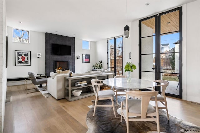 dining area featuring a brick fireplace, a wall of windows, and light hardwood / wood-style floors