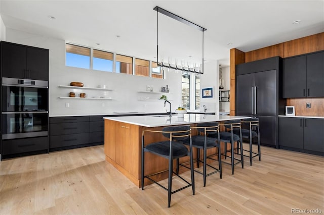 kitchen featuring sink, a center island with sink, a kitchen breakfast bar, paneled fridge, and double oven