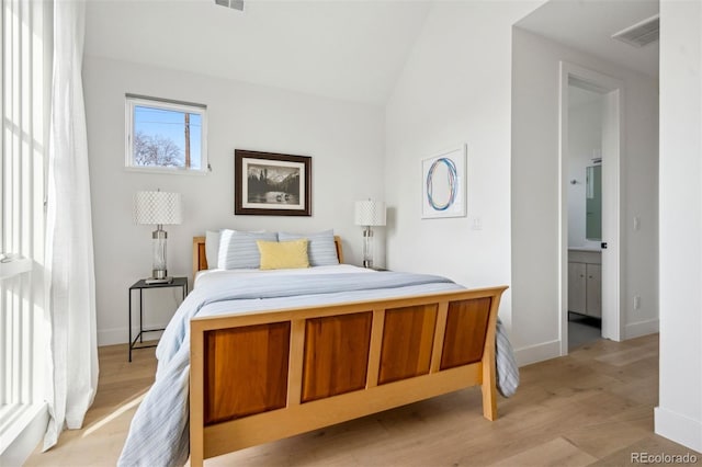 bedroom with connected bathroom, light hardwood / wood-style flooring, and vaulted ceiling