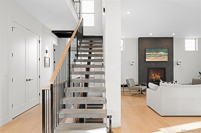 stairs with a brick fireplace, wood finished floors, and recessed lighting