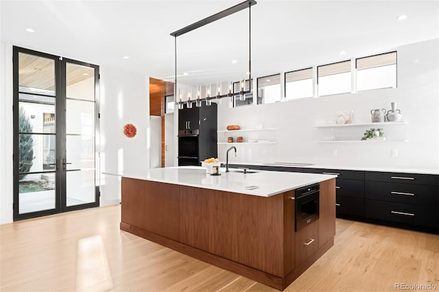 kitchen featuring a sink, light countertops, open shelves, an island with sink, and modern cabinets