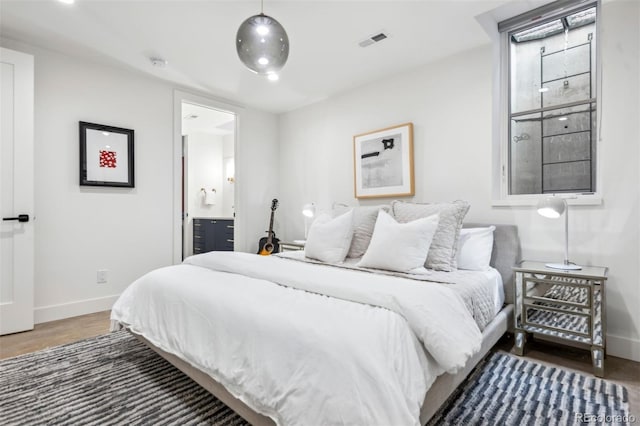 bedroom featuring connected bathroom, wood finished floors, visible vents, and baseboards