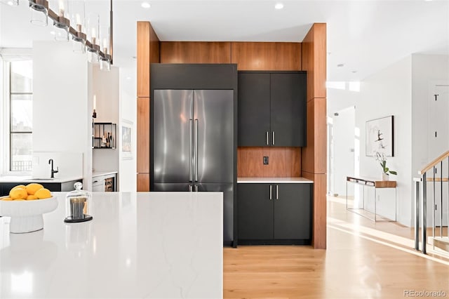 kitchen with high quality fridge, a sink, light wood-style floors, light countertops, and modern cabinets