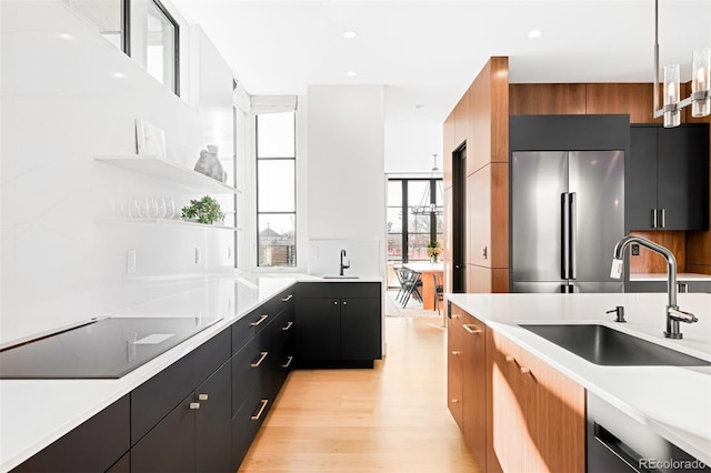 kitchen with black electric stovetop, dark cabinets, a sink, light countertops, and stainless steel fridge