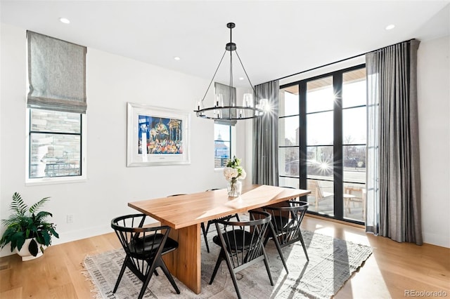 dining space with light wood-type flooring, an inviting chandelier, a wall of windows, and recessed lighting