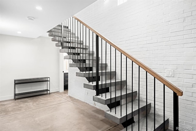 stairway with baseboards, brick wall, recessed lighting, and finished concrete floors