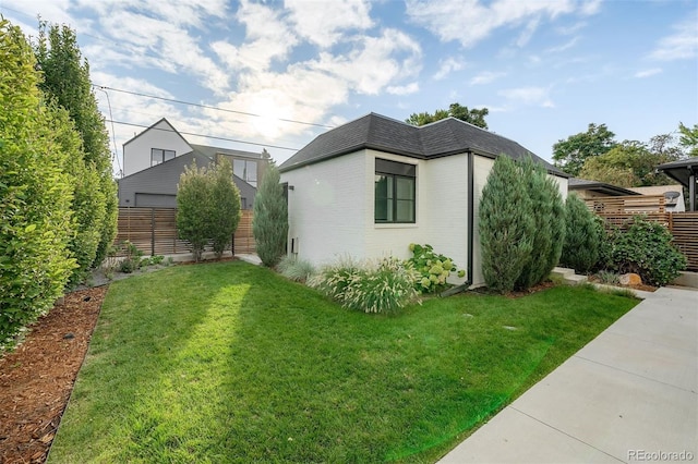 view of home's exterior with a shingled roof, mansard roof, fence, a yard, and brick siding