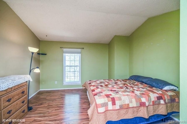 bedroom featuring vaulted ceiling, hardwood / wood-style floors, and a textured ceiling