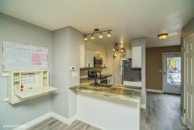 kitchen with appliances with stainless steel finishes, white cabinets, light stone counters, and kitchen peninsula