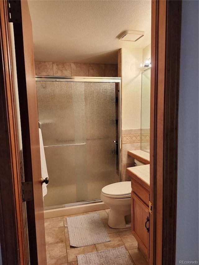full bath featuring tile walls, vanity, a stall shower, a textured ceiling, and wainscoting