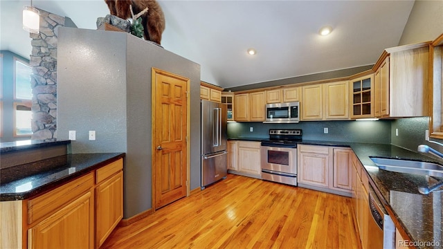 kitchen with stainless steel appliances, a sink, light wood-type flooring, dark stone countertops, and glass insert cabinets