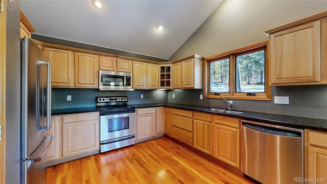 kitchen featuring light wood finished floors, decorative backsplash, lofted ceiling, appliances with stainless steel finishes, and a sink