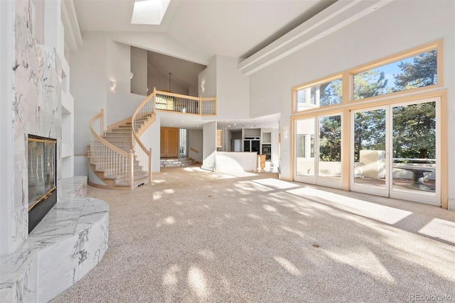 23655 Currant Dr, Golden, CO 80401 - unfurnished living room with a high end fireplace, high vaulted ceiling, stairway, carpet floors, and a skylight