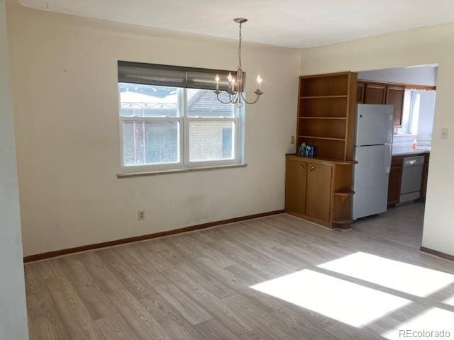 unfurnished dining area with plenty of natural light, an inviting chandelier, and light hardwood / wood-style flooring