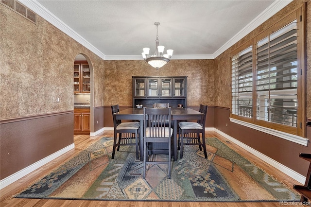 dining area featuring a wainscoted wall, a chandelier, wood finished floors, visible vents, and arched walkways