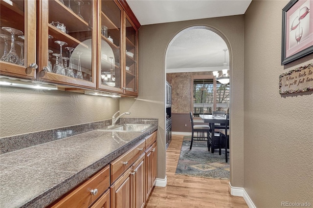 bar featuring a sink, light wood finished floors, baseboards, arched walkways, and a textured wall