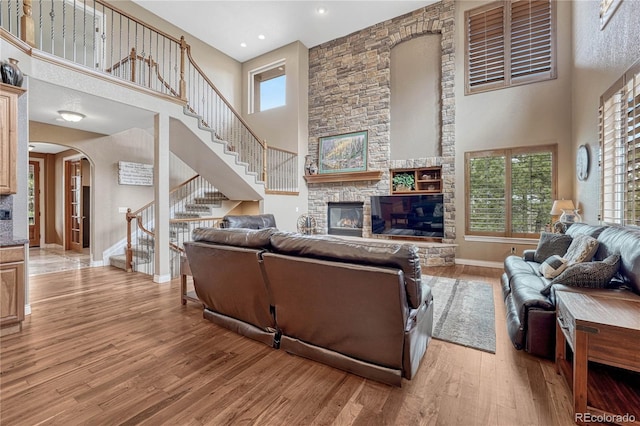 living area featuring arched walkways, stairway, light wood-style floors, and a stone fireplace