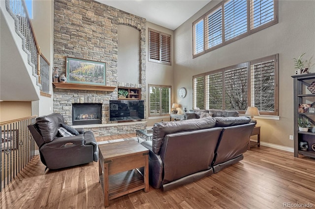 living room with baseboards, a high ceiling, wood finished floors, and a stone fireplace