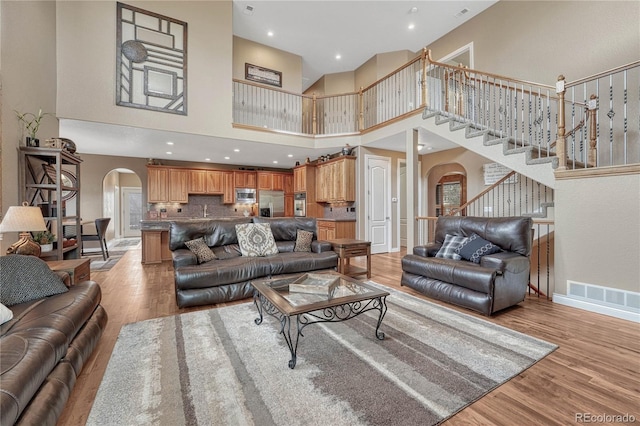 living area featuring stairs, visible vents, arched walkways, and light wood-type flooring